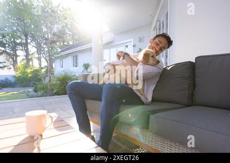 Man sitting on outdoor sofa, hugging dog and enjoying morning sunlight Stock Photo
