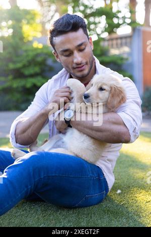 Man sitting on grass, cuddling and playing with golden retriever puppy Stock Photo