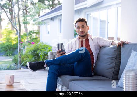 Sitting on outdoor sofa, man holding smartphone and relaxing at home Stock Photo