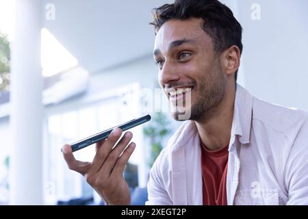 Smiling man holding smartphone and using voice assistant at home Stock Photo