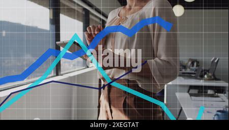 Image of statistical data processing over mid section of woman using digital tablet at office Stock Photo