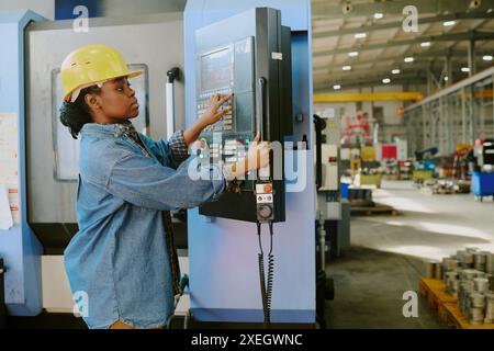 Medium shot of young African American woman working in factory adjusting settings on CNC machine, copy space Stock Photo