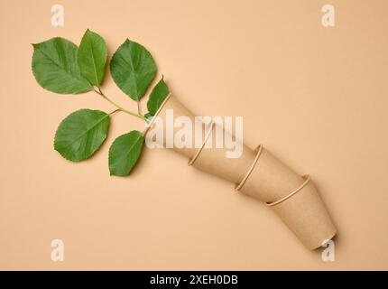 Stack of brown paper disposable cardboard cups on beige background and green leaves Stock Photo