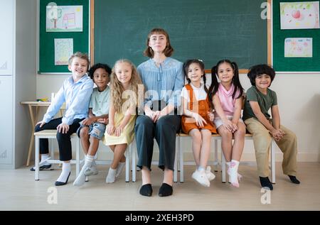 Portrait of a teacher and kids in a classroom where children have pleasure learning. Stock Photo