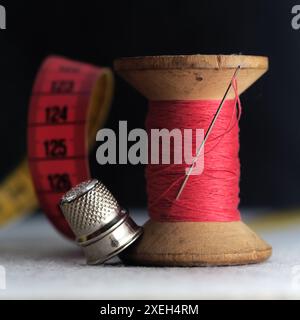 Wooden vintage spool of red thread, needle, metal thimble on abstract backgrouund Stock Photo