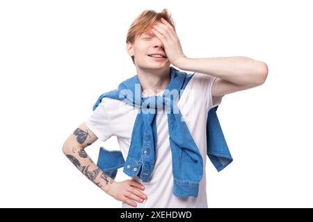 Young positive red-haired man with a short haircut with a tattoo on his arms wearing a white t-shirt Stock Photo