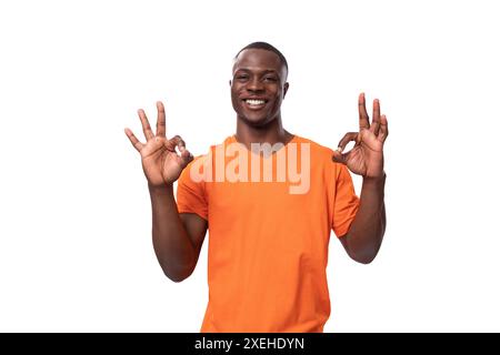 Young african man dressed in orange t-shirt shows ok gesture and smiles Stock Photo