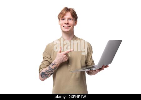 A young red-haired guy in glasses and a brown shirt holds a laptop in his hands. IT specialist stands with equipment Stock Photo