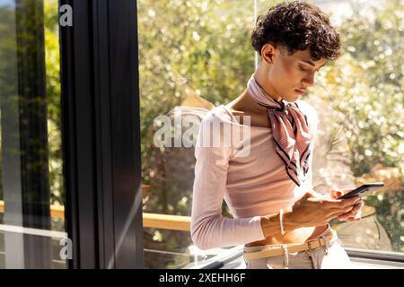 Using smartphone, young young man standing by window, focusing on screen Stock Photo