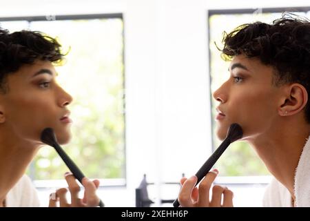 Applying makeup, transgender woman using brush and looking in mirror at home Stock Photo