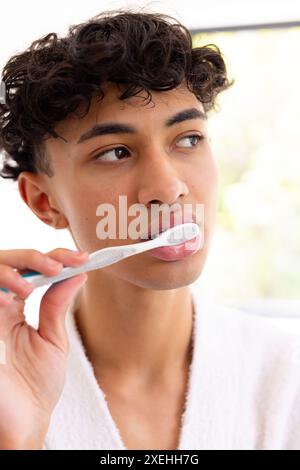 Brushing teeth, young young man in white robe focusing on oral hygiene Stock Photo