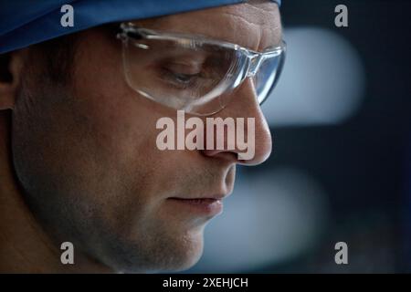 Extreme closeup portrait of focused surgeon wearing protective glasses looking down in operating room copy space Stock Photo