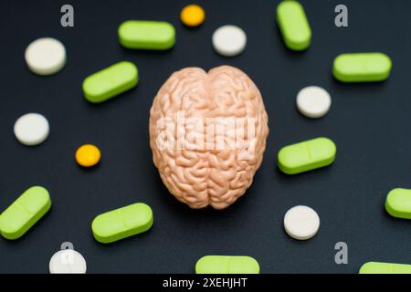 Clay brain model surrounded by variously colored pills on a black surface. Mental health, medical treatment, neuroscience, and pharmacology concept. Stock Photo