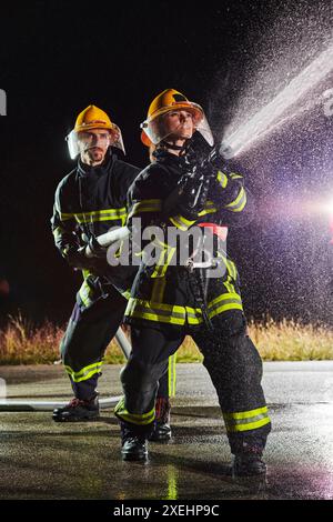 Firefighters using a water hose to eliminate a fire hazard. Team of female and male firemen in dangerous rescue mission. Stock Photo