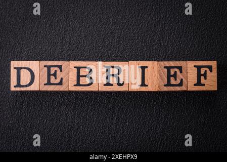 The inscription debrief in wooden cubes on a dark concrete background Stock Photo