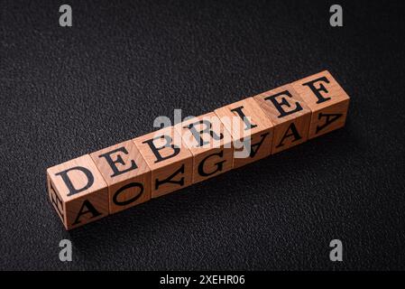 The inscription debrief in wooden cubes on a dark concrete background Stock Photo