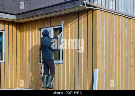 Outdoor work on window openings, roofer installs metal window slopes on facade of frame panel country house. Stock Photo