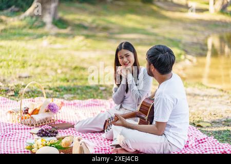 In love couple enjoying picnic time playing guitar in park outdoors Picnic. happy couple relaxing togetherÂ with picnic Basket Stock Photo