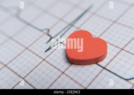 Closeup image of a red heart on a electrocardiogram (ECG) printout. The ECG graph shows a normal sinus rhythm. Healthy heart, wellbeing concept. Stock Photo