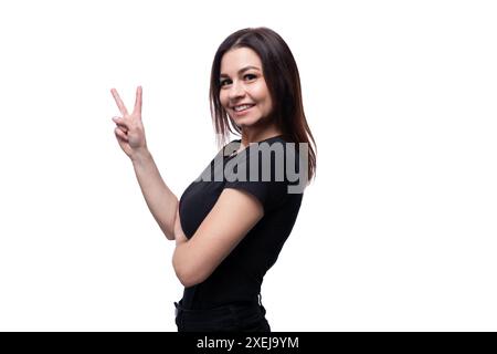 Young confident woman with brown eyes dressed in a black T-shirt shows a greeting gesture Stock Photo