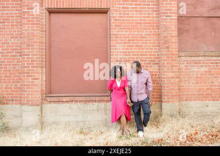 Couple leaning against red brick wall laughing Stock Photo