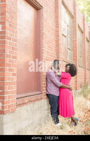 Black couple holding each other leaning against brick wall Stock Photo