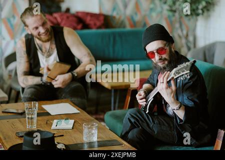 Cheerful bearded man with notepad in hands watching his friend playing guitar and composing new song Stock Photo