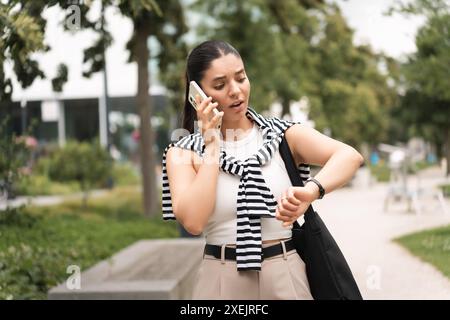 A young woman, dressed in business casual attire, talks on her phone while walking through the city. With a tote bag, she embodies the blend of Stock Photo