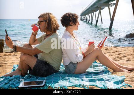couple on the beach browsing smartphones apps. Stock Photo