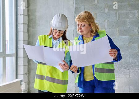Two female industrial workers with technical plan at construction site Stock Photo