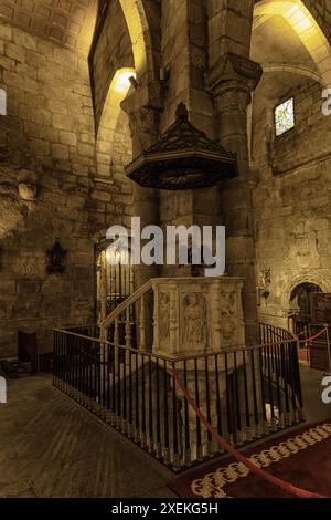 The serene interior of the Basilica of Santa Eulalia in Merida, Spain, featuring stone arches, wooden pews, and a beautifully illuminated altar. Stock Photo