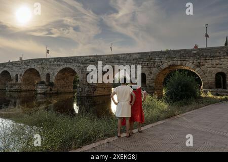 Two reenactors dressed in Roman attire stand by the ancient Roman bridge over the Guadiana River in Merida, Spain. The scene captures the historical a Stock Photo