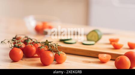 Slicing cherry tomatoes and cucumbers on a wooden cutting board Stock Photo