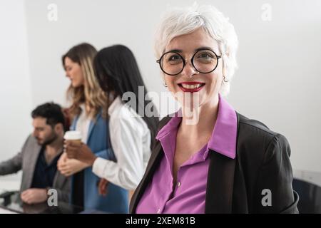 Confident senior businesswoman with a team in the background - showcasing leadership and professionalism, diverse office environment, modern workplace Stock Photo
