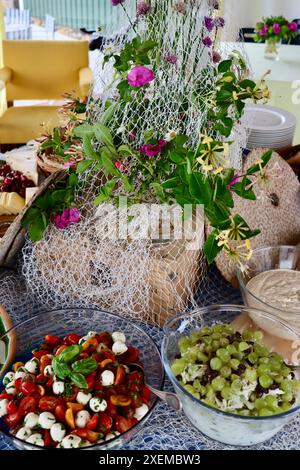 Mozzarella salad and Waldorf salad on buffet dinner decorated with old fishing net, wild roses and wild onion flowers.  Midsummer in Sweden, June 2024 Stock Photo