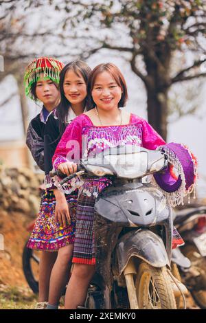 Three young Vietnamese women posing together on a motorcycle, wearing traditional dresses; Ban Nam Nghiep, Muong La, Son La, Vietnam Stock Photo