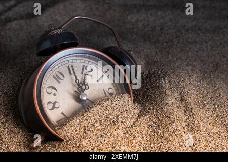 Alarm clock in sand on dark background. Time concept Stock Photo