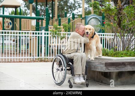 Man in a wheelchair showing deep appreciation for his service dog while spending time together outdoors Stock Photo