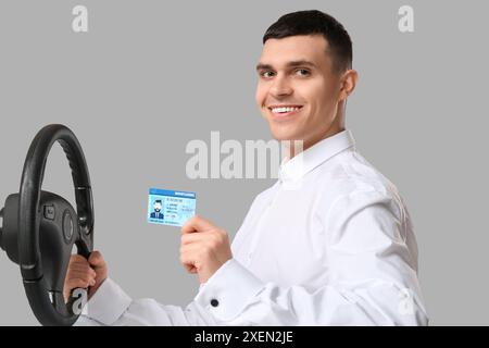 Young happy man holding driver license and steering wheel on grey background Stock Photo