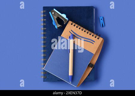 Notebooks, pen, stapler and clothespin on blue background Stock Photo