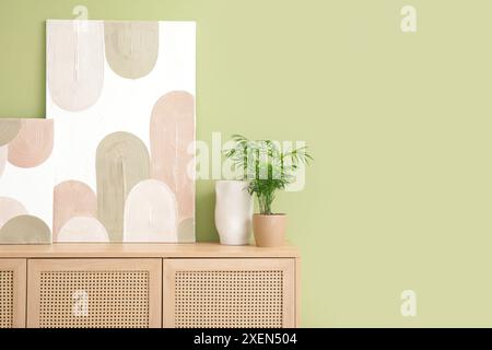 Wooden chest of drawers, houseplant and beautiful pictures on green wall in room Stock Photo