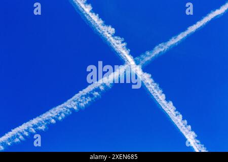 Two airplane exhaust trails forming an 'X' in the blue sky; Calgary, Alberta, Canada Stock Photo