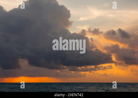Sun setting behind dramatic clouds over the ocean at Mai Khao Beach in North Phuket; Mai Khao, Phuket, Thailand Stock Photo