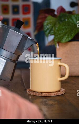 Pouring coffee from a moka pot into a enamel cup Stock Photo