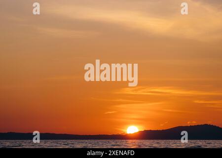 Glowing sun sinking behind the horizon on the silhouetted island of Bunaken in the Celebes Sea, Indonesia; Bunaken, North Sulawesi, Indonesia Stock Photo