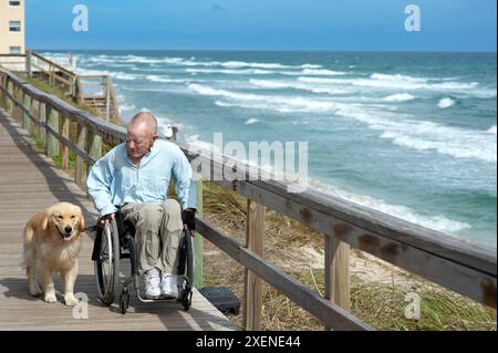 Paraplegic man in a manual wheelchair and his service dog enjoy walking along the ocean promenade; Boynton Beach, Florida, United States of America Stock Photo