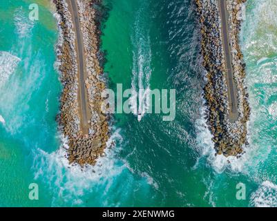 Aerial view of a small boats heading out to sea between breakwater walls at Narooma on the South Coast of New South Wales, Australia. Stock Photo