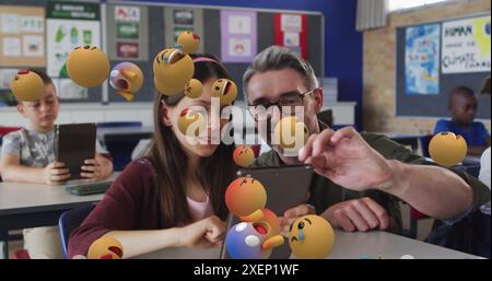 Image of emoticons over diverse male teacher helping girl in using digital tablet in classroom Stock Photo