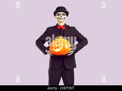 Scary man with traditional Halloween skeleton make-up and gloves holding glowing pumpkin in hands. Stock Photo