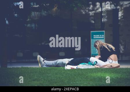 A woman sits on some grass with her partner lying down with his head resting in her lap Stock Photo
